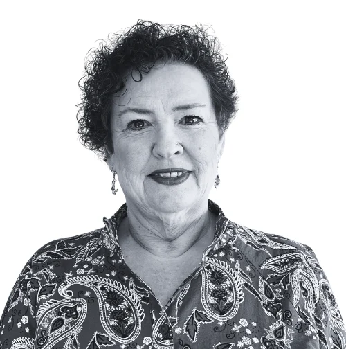 Mel, a woman with short curly hair wearing a patterned shirt, smiles at the camera.
