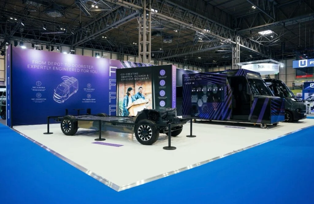 A trade show booth displays a vehicle chassis and a finished electric delivery van.