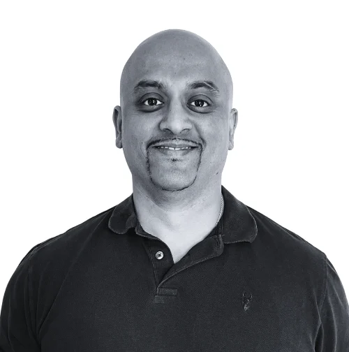 A smiling man with a shaved head and a goatee wearing a black polo shirt.