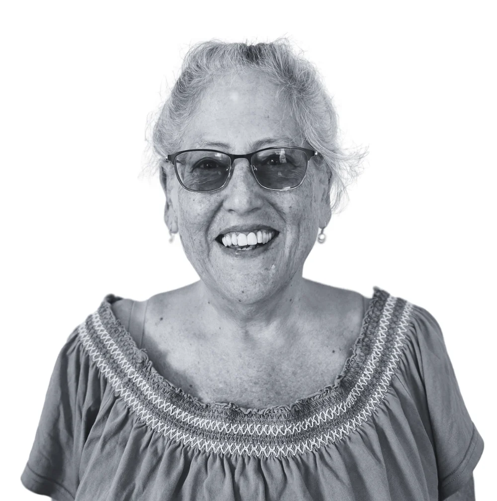 A smiling older woman with glasses and light hair wears a textured top against a white background.