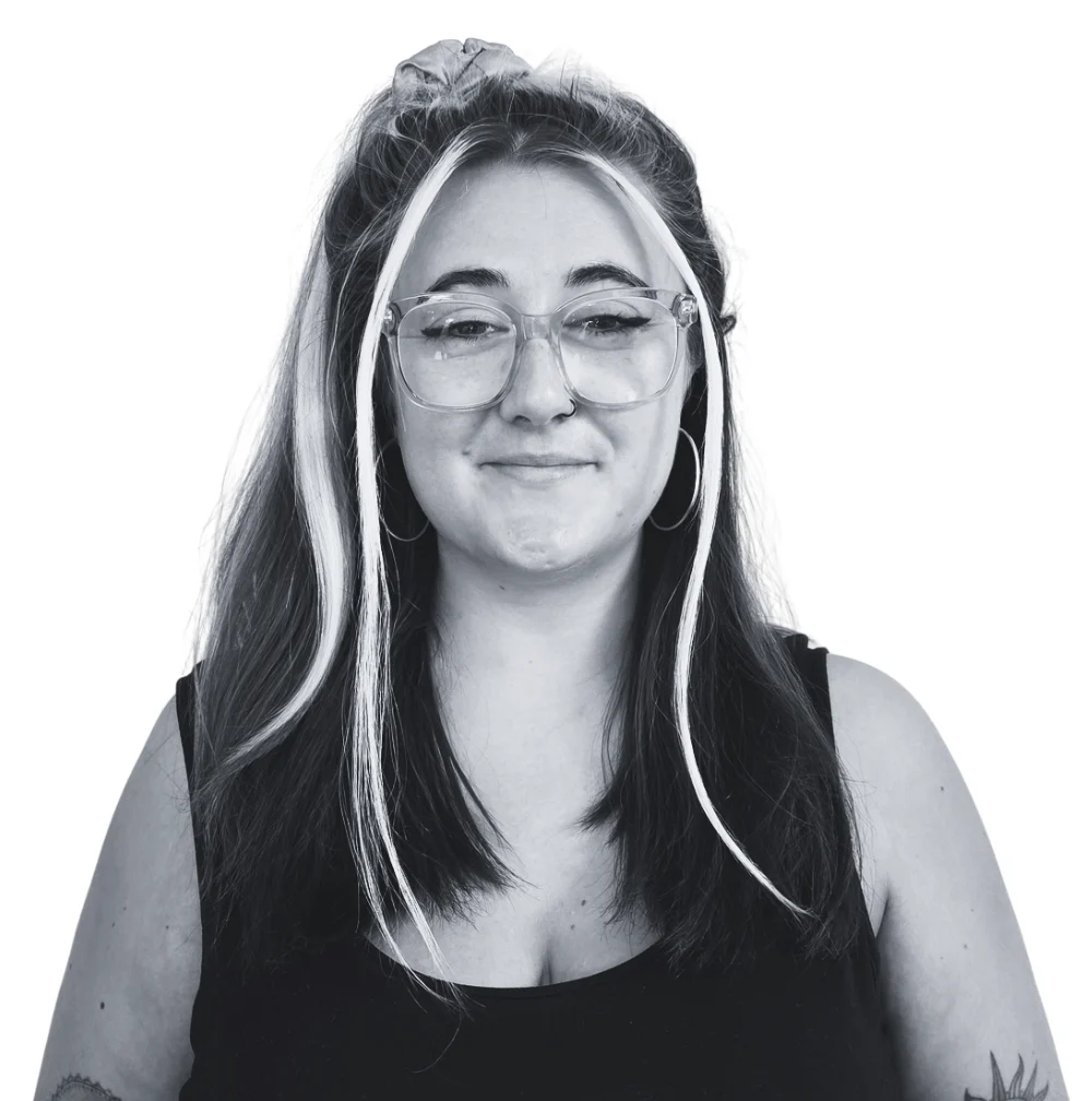 A young woman with glasses and highlighted hair smiles against a white background.