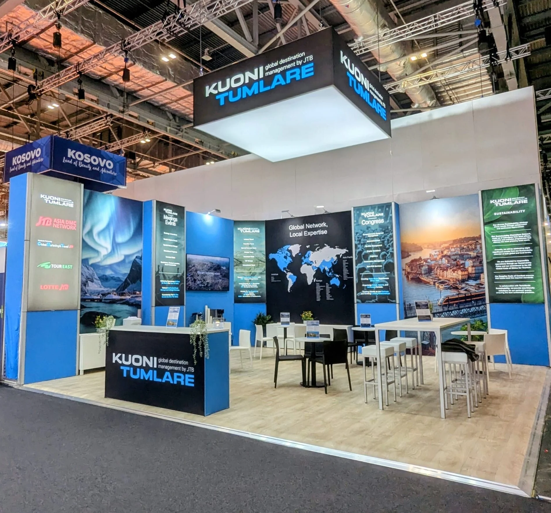 Kuoni Tumlare trade show booth featuring a large overhead sign, world map display, and seating area.
