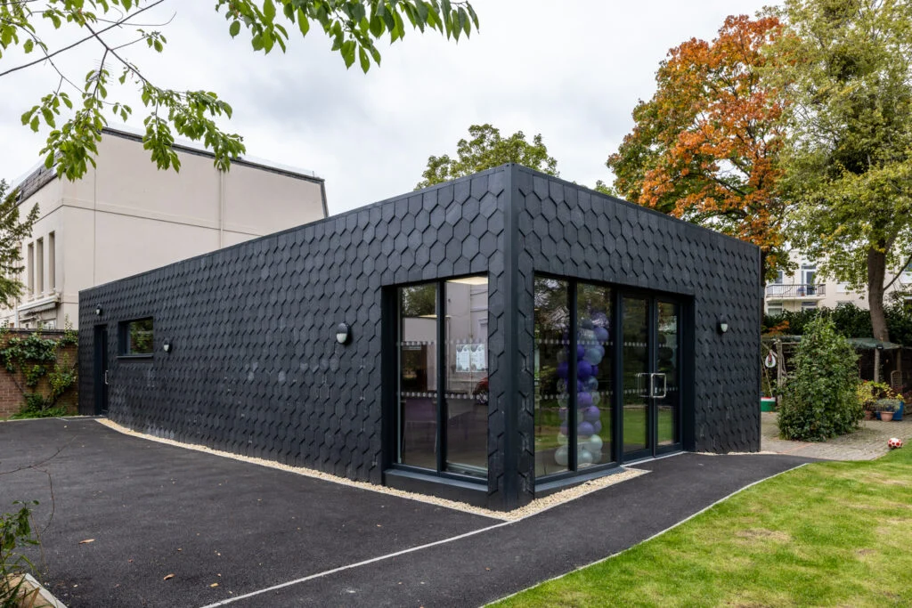Modern single-story building with black hexagonal exterior tiles and large glass windows.