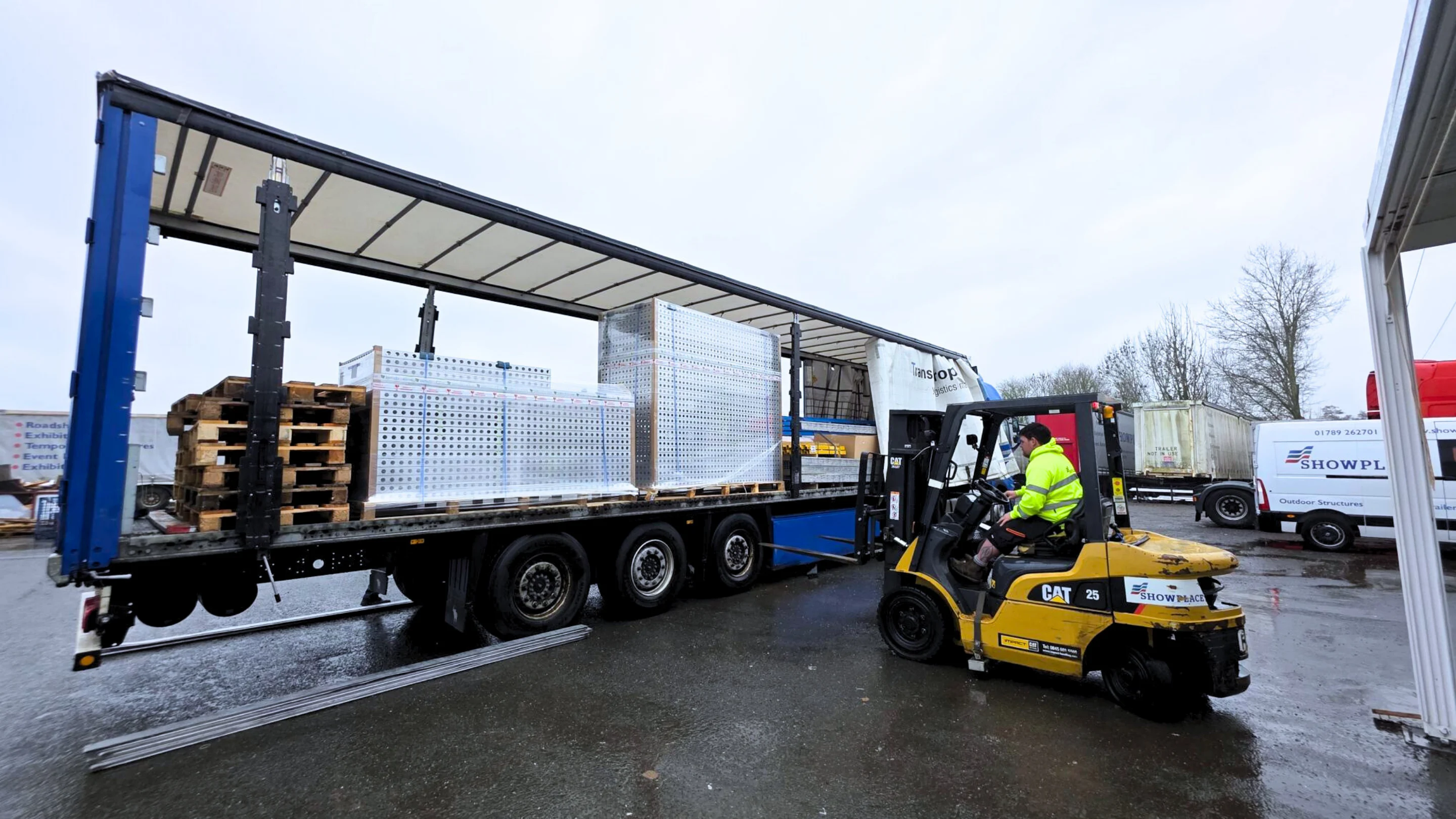 A forklift operator loads palletized equipment onto a flatbed trailer.