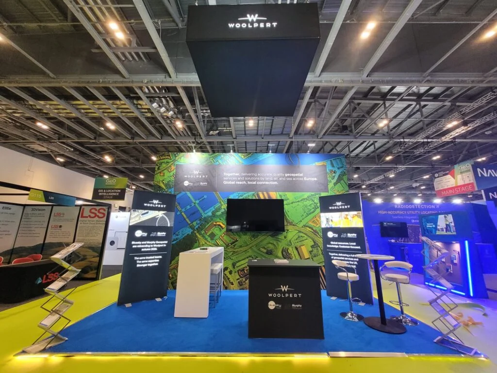 Woolpert trade show booth featuring a branded display, information kiosks, and seating on a blue carpet.
