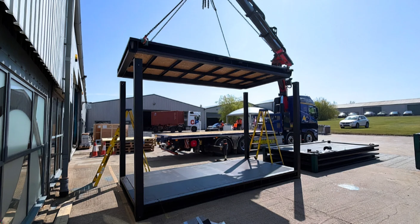 A crane lifts a modular building frame into position at a construction site.