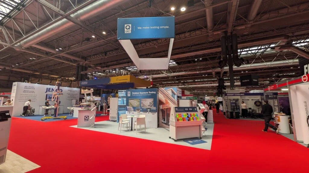 Q-Lab trade show booth featuring outdoor weathering testing equipment on a red carpet floor.