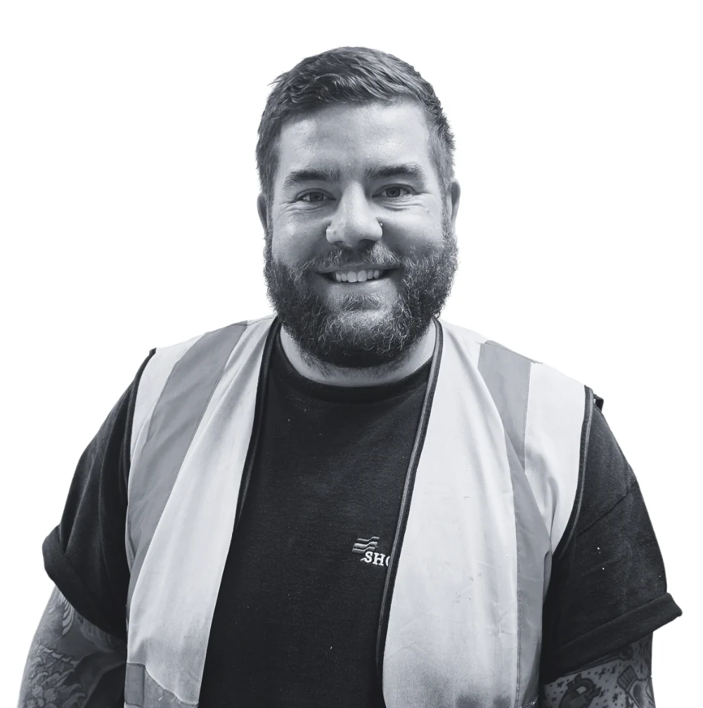 A smiling man with a beard wearing a high-visibility vest over a black t-shirt.
